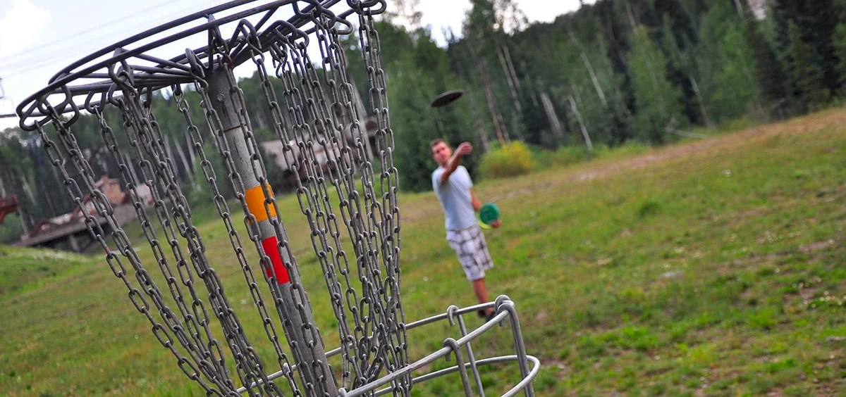 image of a disc golf basket with a player throwing toward it | Telluride